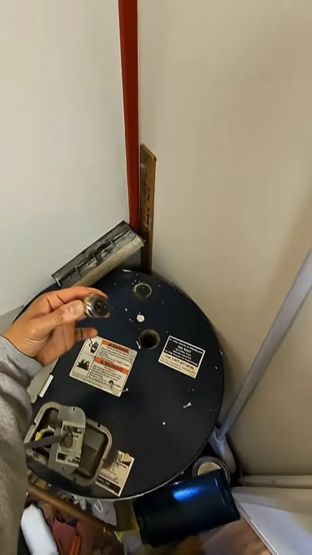 Hand holding a small part above the open top of a dark blue storage tank, shown for tank top inspections in Littleton homes