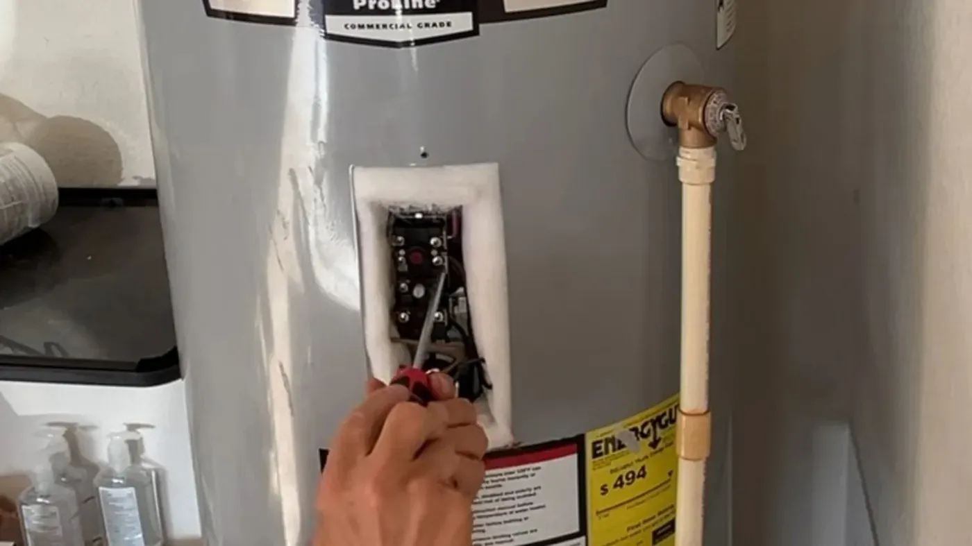 Screwdriver inside the open thermostat compartment of an electric storage tank, used for thermostat checks in Littleton homes