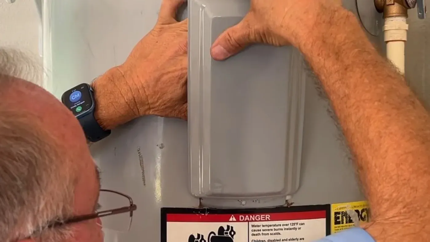 Technician lifting the thermostat access cover on an electric storage tank, shown for local hot water care in Littleton, CO